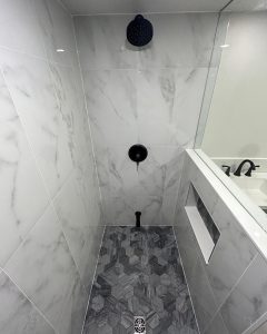 Modern bathroom shower with white marble tiles, gray hexagon floor tiles, black fixtures - GTA