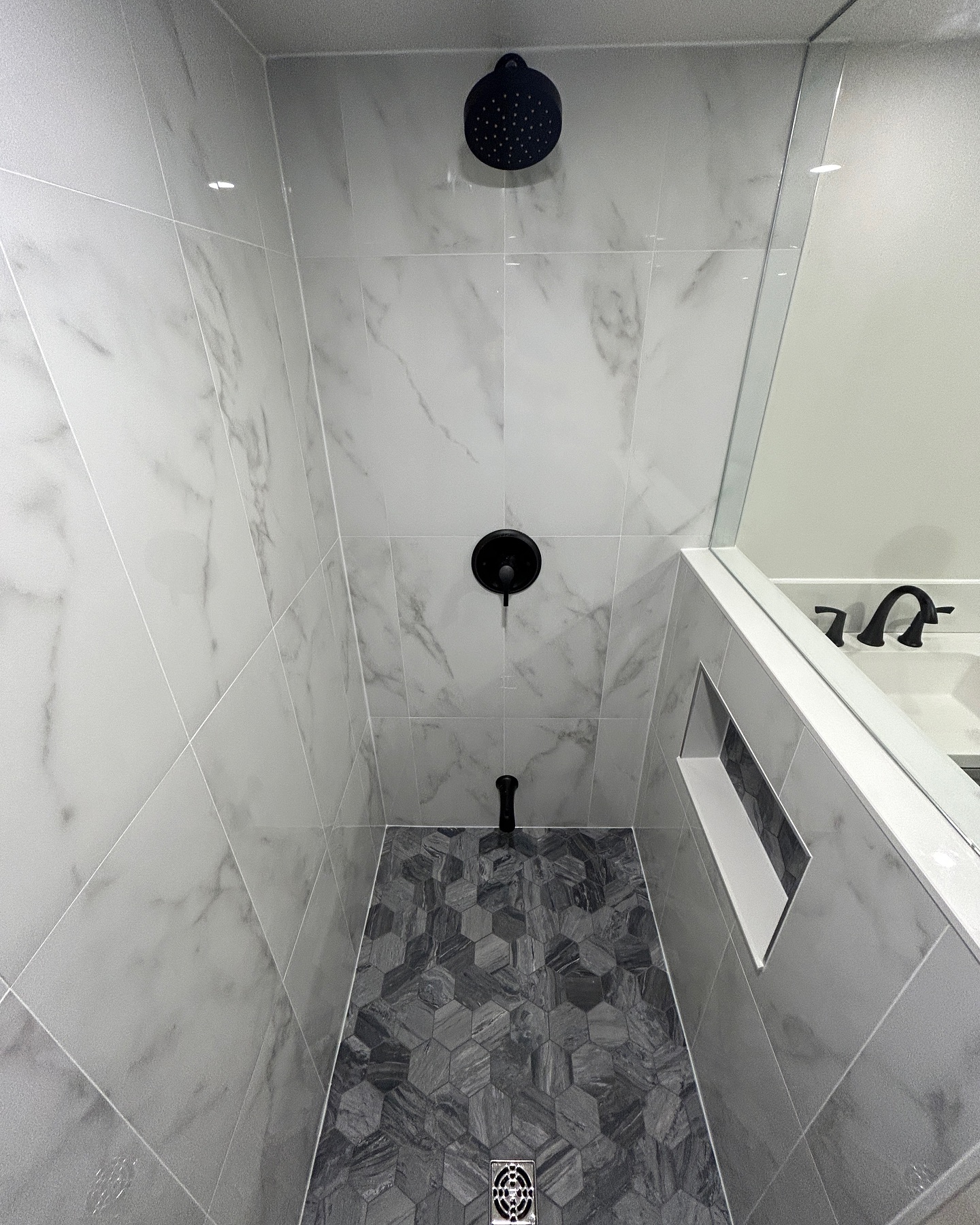 Modern bathroom shower with white marble tiles, gray hexagon floor tiles, black fixtures - GTA